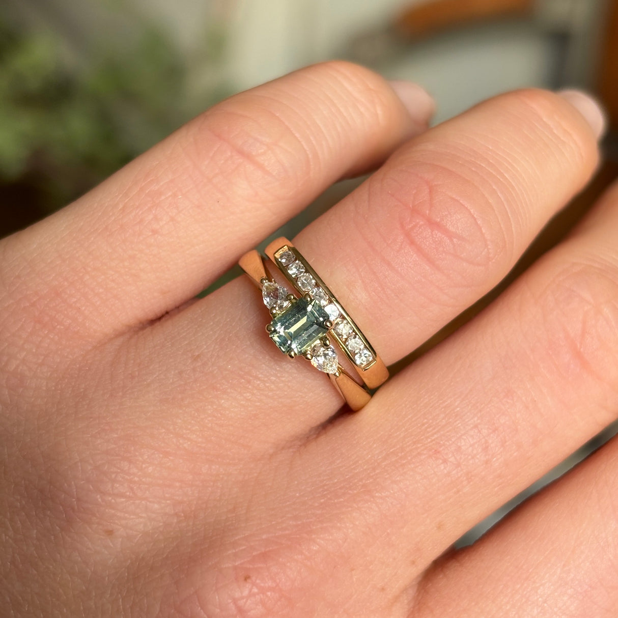 Green sapphire and diamond three-stone engagement ring worn on the hand alongside gold bands, demonstrating scale and styling.