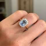 Antique-inspired, blue oval sapphire and diamond cluster engagement ring in yellow gold on a hand