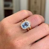 Antique-inspired, Sky blue sapphire and diamond cluster engagement ring in yellow gold.  Worn on a hand with a wedding band to show the wedding fit of the ring. 