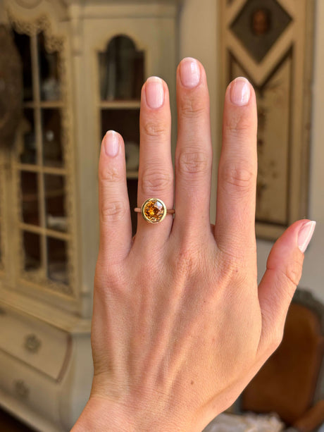 Antique-inspired, honeyed-orange zircon solitaire ring in yellow gold worn on a hand against an antique interiors backdrop