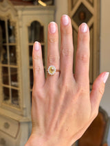 Antique-inspired, vibrant yellow sapphire and diamond cluster engagement ring in yellow gold worn on a hand against a blurred background. 