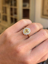 Gold antique-inspired engagement ring with a large yellow sapphire and a halo of smaller diamonds on a hand.