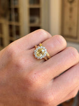 Gold Antique-inspired, yellow sapphire and diamond cluster engagement ring on a hand against a blurred background