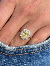 Antique-inspired, yellow sapphire and diamond halo gold engagement ring on a finger wearing blue jeans.