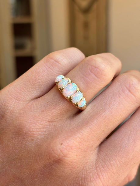 An Antique, Victorian yellow gold ring featuring five opal gemstones in a row, worn on a person's finger. The opal stones exhibit a milky white color with hints of blue and green.