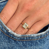 Gold Vintage-inspired, princess-cut diamond rub-over solitaire engagement ring on a person's finger wearing blue jeans.