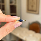 Hand holding a Vintage, 1960s blue sapphire & diamond three-stone engagement ring in yellow gold against a blurred indoor background