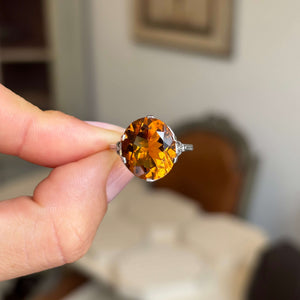 Hand holding a platinum Antique, Art Deco citrine cocktail ring against a blurred indoor background