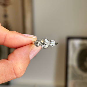 Hand holding an Antique, Art Deco old-cut diamond three-stone platinum ring against a blurred background