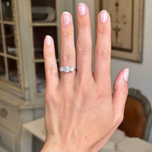 Hand wearing an Antique, Art Deco diamond three-stone platinum ring on a blurred indoor background