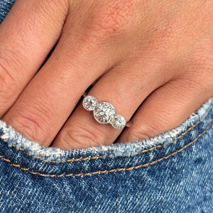 Antique, Art Deco diamond three-stone engagement ring in platinum worn on a finger wearing blue jeans