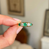 an Antique Victorian yellow gold five stone engagement ring, held by a hand to showcase the three emeralds and two old mine diamonds. 