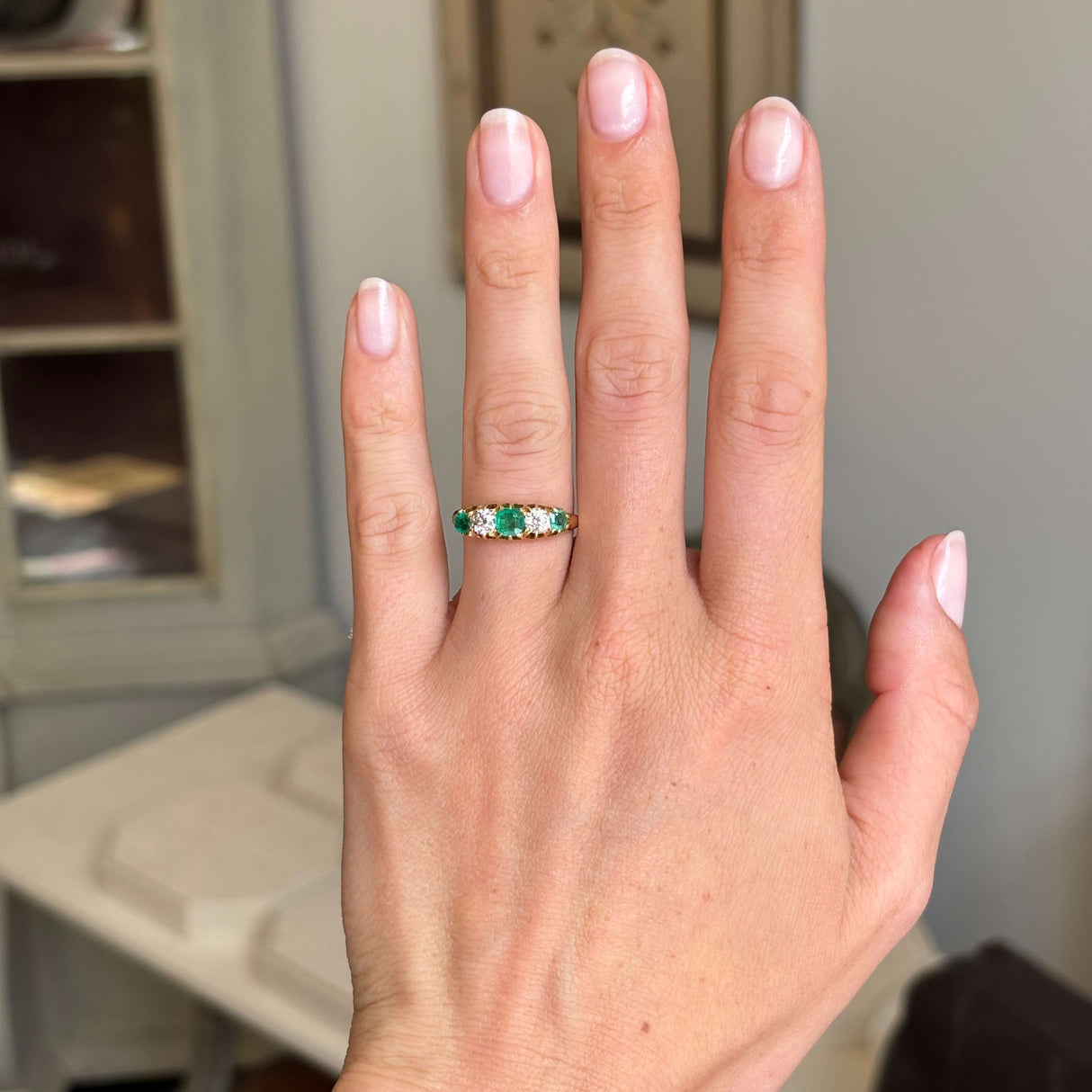 Hand wearing an Antique, Victorian emerald & old-mine diamond five-stone ring in yellow gold with a neutral background