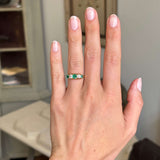 Hand wearing an Antique, Victorian emerald & old-mine diamond five-stone ring in yellow gold with a neutral background