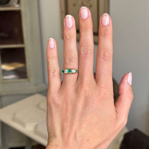 Hand wearing an Antique, Victorian emerald & old-mine diamond five-stone ring in yellow gold with a neutral background