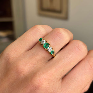 Gold Antique, Victorian emerald & old-mine diamond five-stone engagement ring on a hand against a neutral background