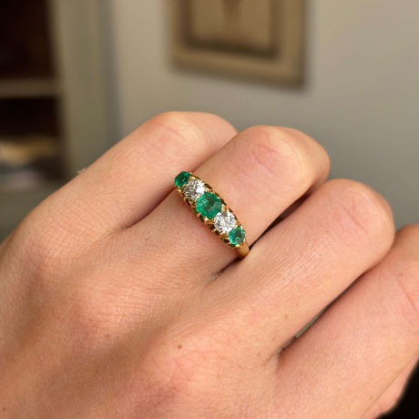 Gold Antique, Victorian emerald & old-mine diamond five-stone engagement ring on a hand against a neutral background