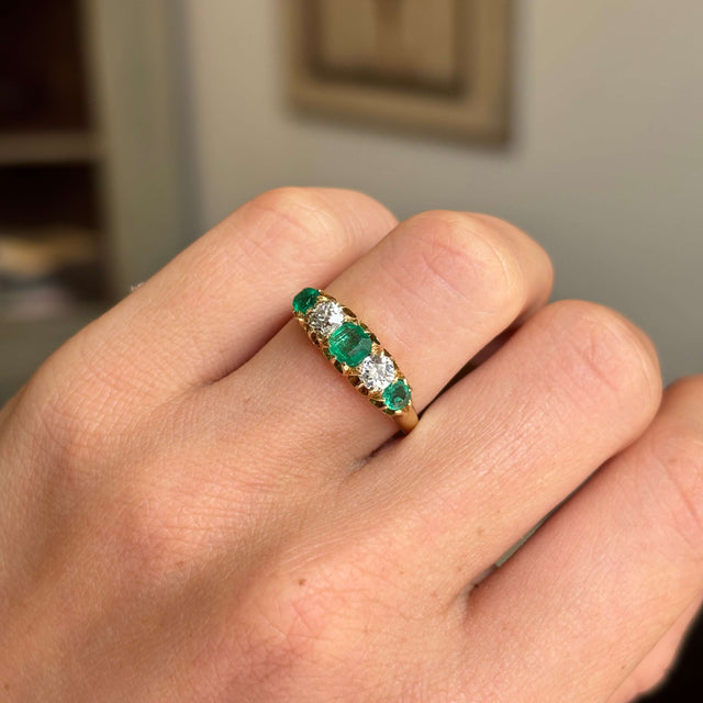 Gold Antique, Victorian emerald & old-mine diamond five-stone engagement ring on a hand against a neutral background