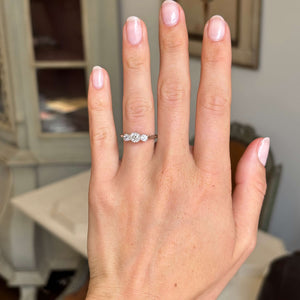 A three-stone old-cut diamond vintage engagement ring set in 18ct white gold displayed on a hand against an interior background