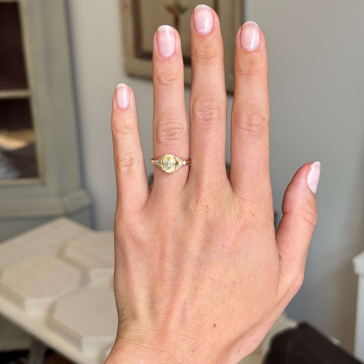 A Vintage-inspired, yellow cushion-cut sapphire and diamond ring in gold worn on a hand against an interiors setting