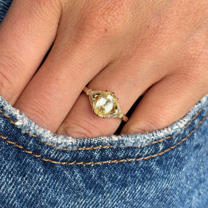 Close up on a hand wearing a Vintage-inspired yellow cushion cut sapphire & diamond engagement ring in yellow gold against a denim background.