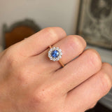 Close-up of a hand wearing an Antique-inspired, electric blue sapphire and diamond cluster engagement ring in gold