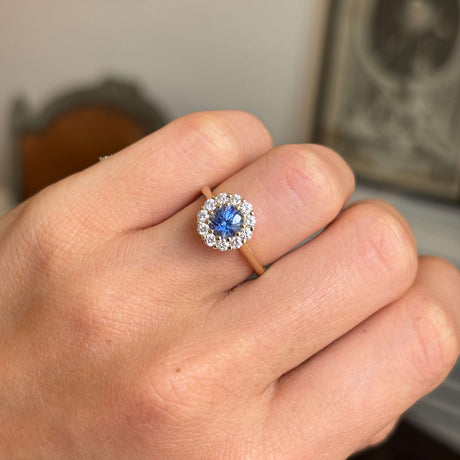 Close-up of a hand wearing an Antique-inspired, electric blue sapphire and diamond cluster engagement ring in gold