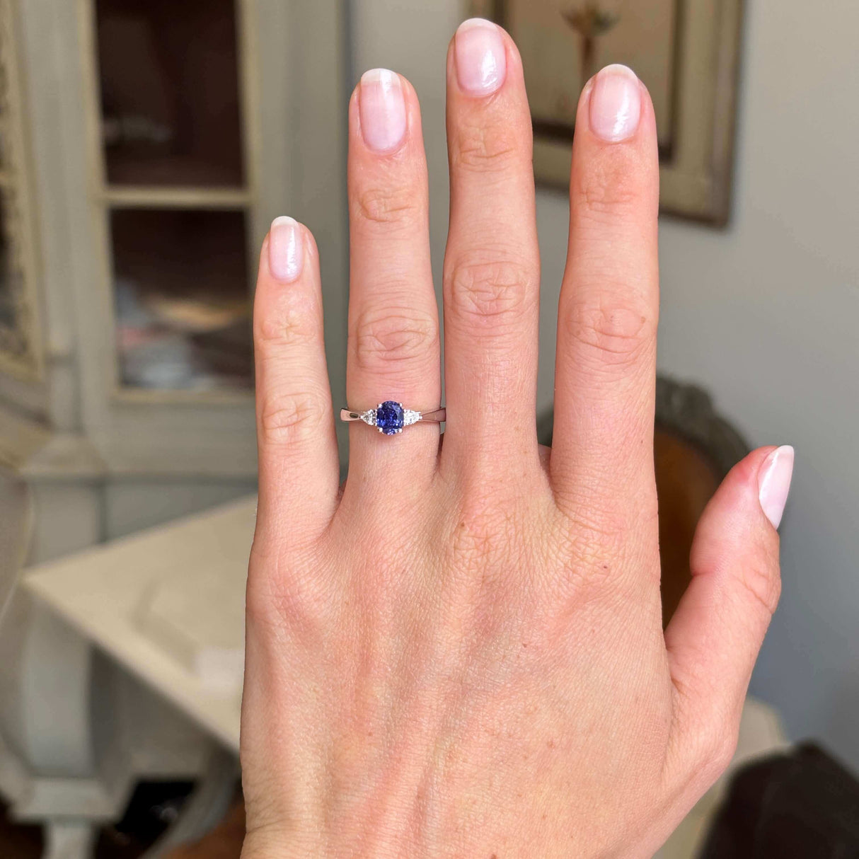 Hand wearing a platinum vintage-inspired, indigo sapphire & diamond three-stone engagement ring