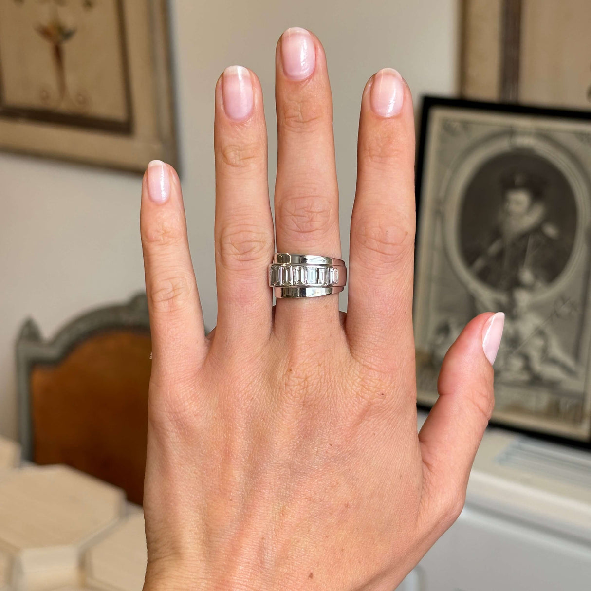 Hand wearing a platinum Vintage, 1940s channel-set baguette-cut diamond ring on a blurred indoor background