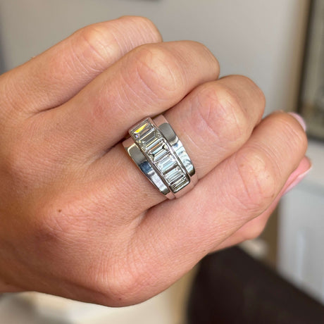 Close up of a hand wearing a Vintage, 1940s channel-set baguette-cut diamond ring in platinum on a neutral background