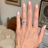 A close-up of a person's hand wearing Antique-inspired, blue sapphire and diamond cluster engagement ring in yellow gold. 