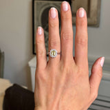 Hand wearing a platinum Antique-inspired, yellow sapphire and diamond cluster engagement ring, with a blurred background.