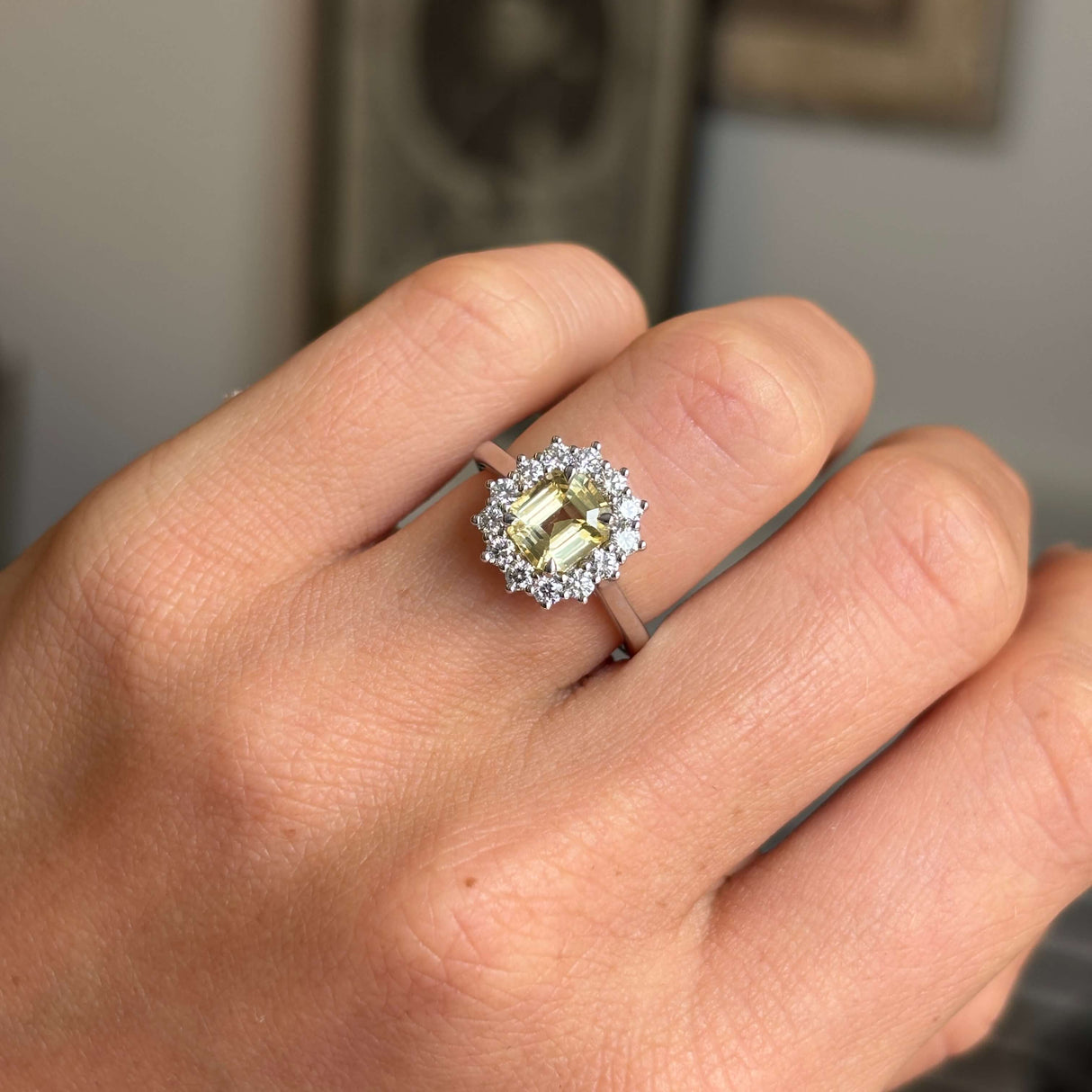 Hand wearing an Antique-inspired ring with a central yellow sapphire surrounded by a halo a diamonds set in platinum on a blurred background