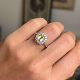 Hand wearing an Antique-inspired ring with a central yellow sapphire surrounded by a halo a diamonds set in platinum on a blurred background