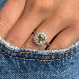 Antique inspired, yellow sapphire and diamond cluster engagement ring in platinum on a person's finger against a denim background