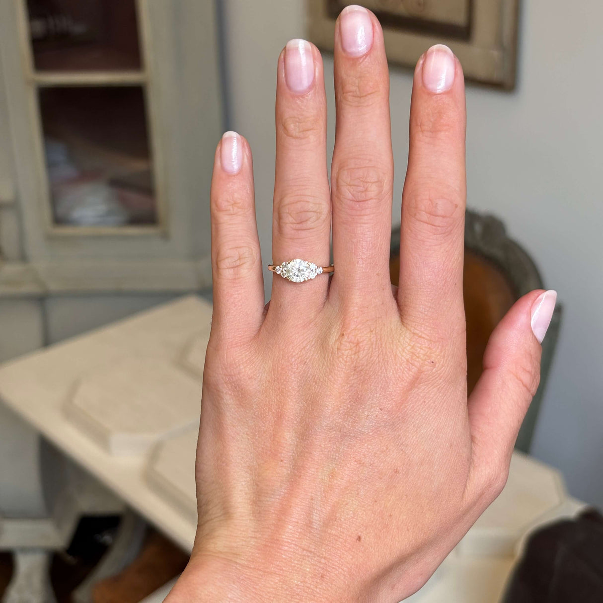 Hand wearing a Antique-inspired, cloudy diamond cluster trefoil ring with a blurred indoor background