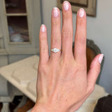 Hand wearing a Antique-inspired, cloudy diamond cluster trefoil ring with a blurred indoor background