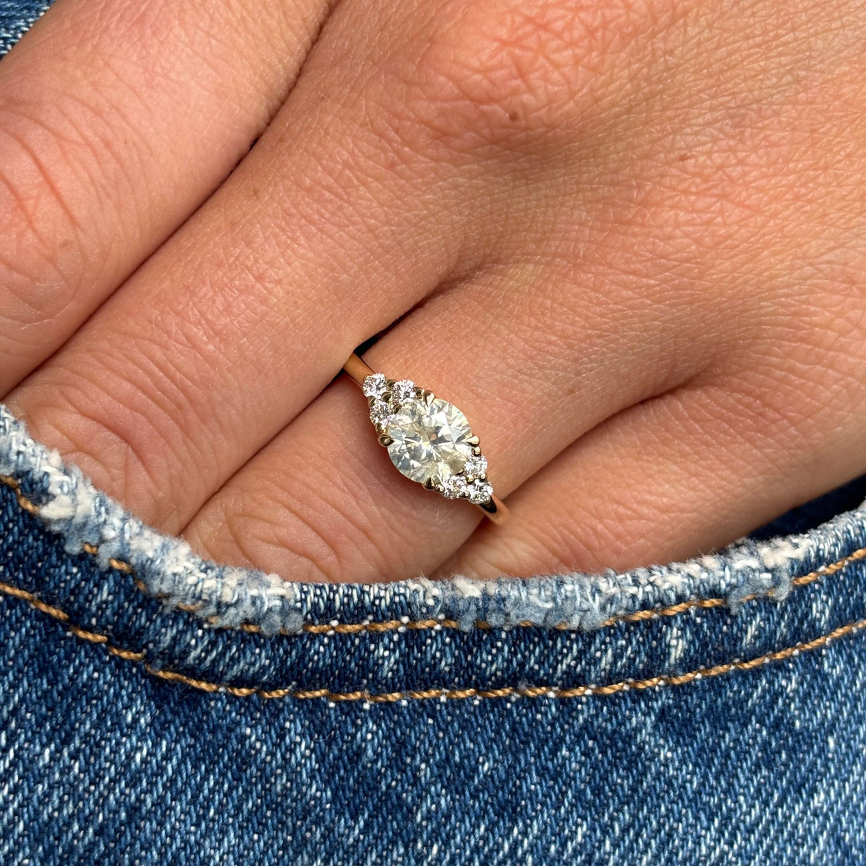 Antique-inspired, cloudy diamond cluster trefoil ring in gold on a finger with a denim background