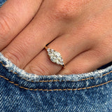 Antique-inspired, cloudy diamond cluster trefoil ring in gold on a finger with a denim background