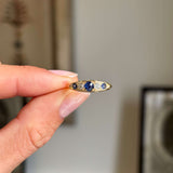 Antique, Victorian sapphire & diamond five-stone engagement ring in gold held by a hand against a neutral background