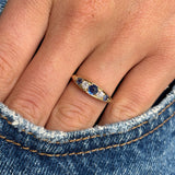 Close-up of a hand wearing an Antique, Victorian sapphire & diamond five-stone engagement ring in gold, against a denim background.