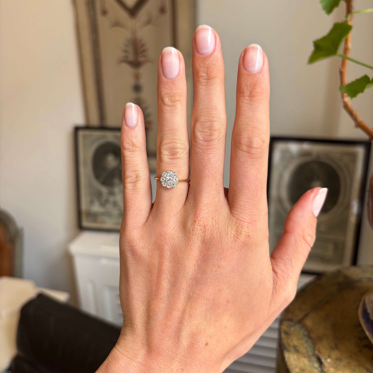 Hand wearing an Antique, Edwardian gold ring featuring nine old-cut diamonds in a daisy cluster arrangement with a decorative background