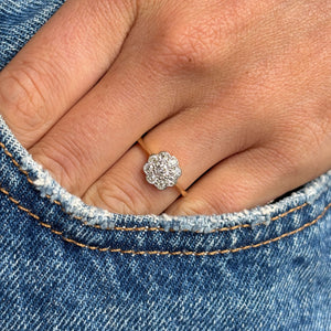 Close-up of a hand wearing a gold Antique, Edwardian old-cut diamond cluster engagement  ring with blue jeans in the background