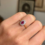 Close-up of a hand wearing a yellow gold Vintage, 1940s ruby and diamond cluster engagement ring on a neutral background