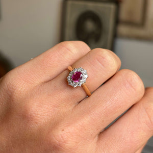 Close-up of a hand wearing a yellow gold Vintage, 1940s ruby and diamond cluster engagement ring on a neutral background