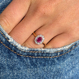 Close-up of a hand wearing a Vintage, 1940s ruby and diamond cluster engagement ring in yellow gold on blue denim fabric.