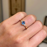 A close-up of a hand wearing an antique-inspired blue sapphire & diamond three-stone engagement ring in yellow gold. 