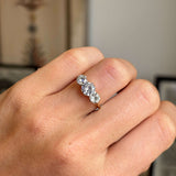Close up of an Antique, Edwardian old-cut diamond three-stone ring, worn on a hand against a blurred interior backdrop
