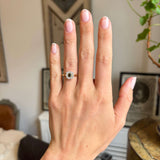 A hand wearing an Antique-inspired, Brown diamond cluster engagement ring in yellow gold, on the wedding finger, set against an interiors background.