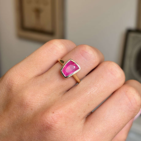 Hand wearing a Vintage-inspired, pink ruby solitaire engagement ring in yellow gold on a neutral background